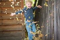 Junge wirft lachend Blätter in die Luft.