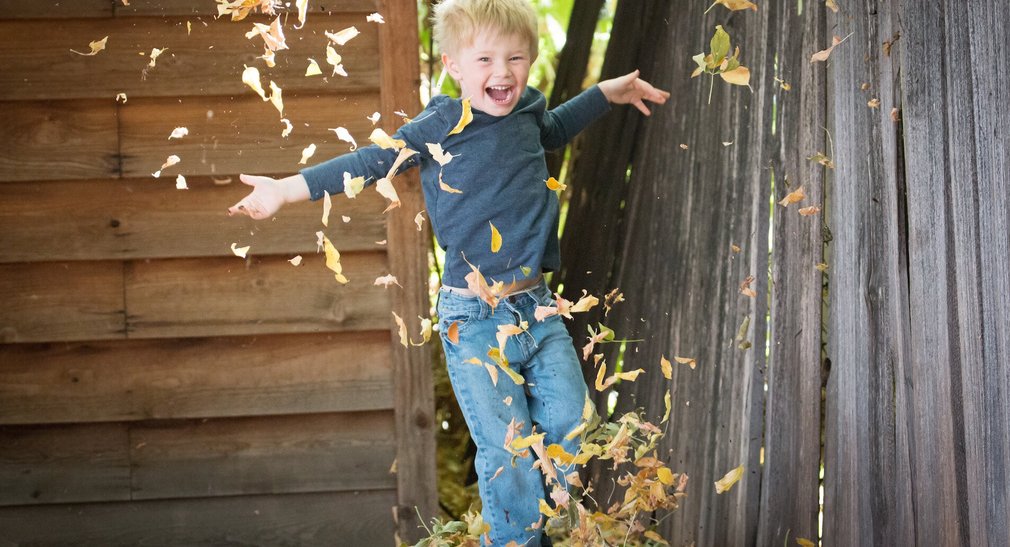 Junge wirft lachend Blätter in die Luft.