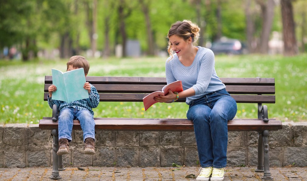 Mutter und Sohn sitzen auf Parkbank und lesen. Mutter zeigt Sohn etwas