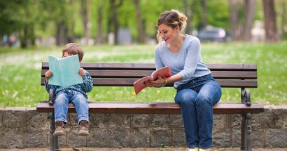 Mutter und Sohn sitzen auf Parkbank und lesen. Mutter zeigt Sohn etwas