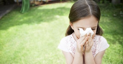 Kita-Kind mit Allergie putzt sich im Garten die Nase