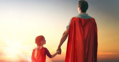 Vater und Kind mit Superhelden-Cape bei Sonnenuntergang