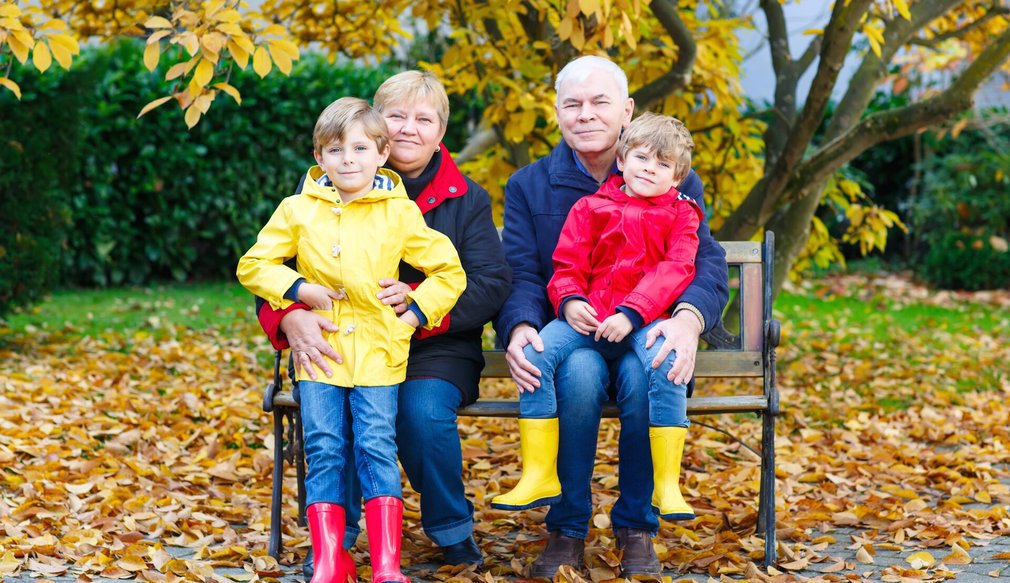 Großeltern und zwei Enkelkinder sitzen in Regensachen auf einer Bank. Herbst.