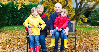 Großeltern und zwei Enkelkinder sitzen in Regensachen auf einer Bank. Herbst.
