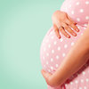 Schwangere Frau im rosa weißgepuntetem Kleid hält sich Bauch.