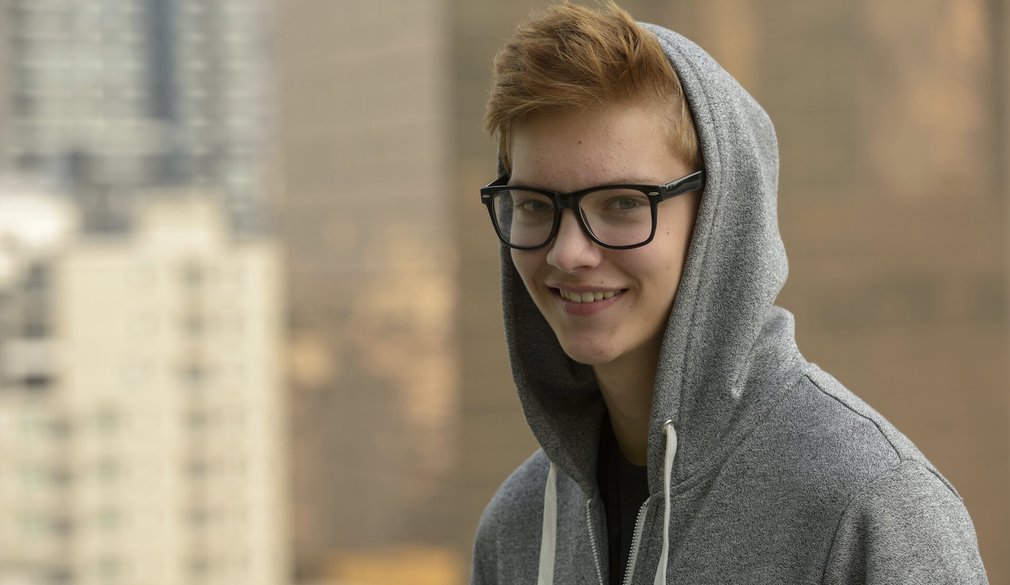 Teenager Junge mit Brille und Kaputzenshirt sieht in die Kamera und lächelt