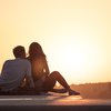 Paar sitzt auf dem Boden und blickt in den Sonnenuntergang