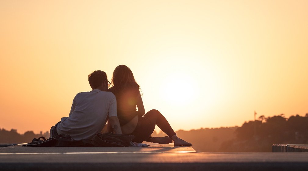 Paar sitzt auf dem Boden und blickt in den Sonnenuntergang