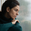 Traurige Frau sitzt mit Kopf am Fenster gelehnt und sieht durch Fensterscheibe mit Regntropfen.