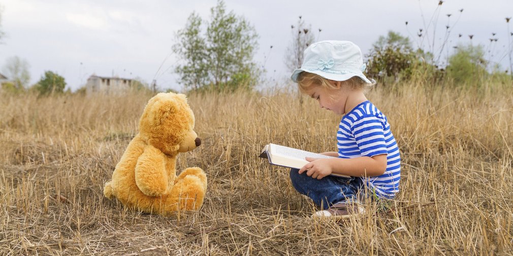 Kind auf Wiese liest Teddybären vor