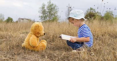 Kind auf Wiese liest Teddybären vor