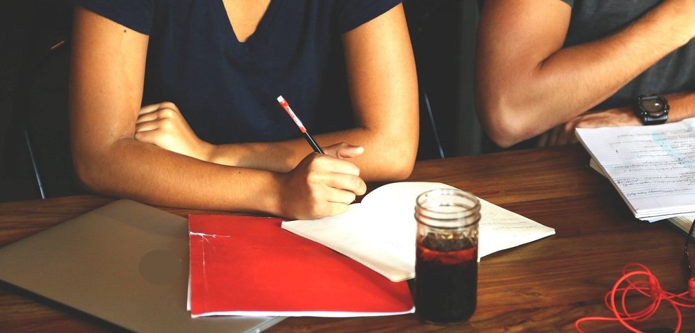 Ausschnitte von zwei Menschen am Tisch mit Block, Laptiop und Stiften.