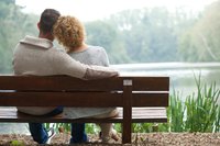Frau und Mann sitzen liebevoll auf Bank. Schauen auf See.