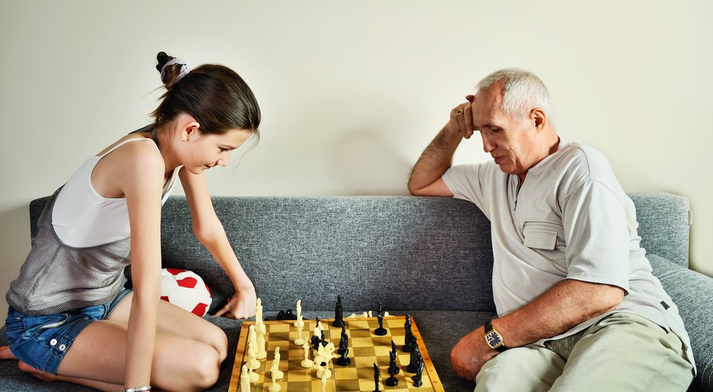 Jugendliche und Großvater spielen Schach auf dem Sofa