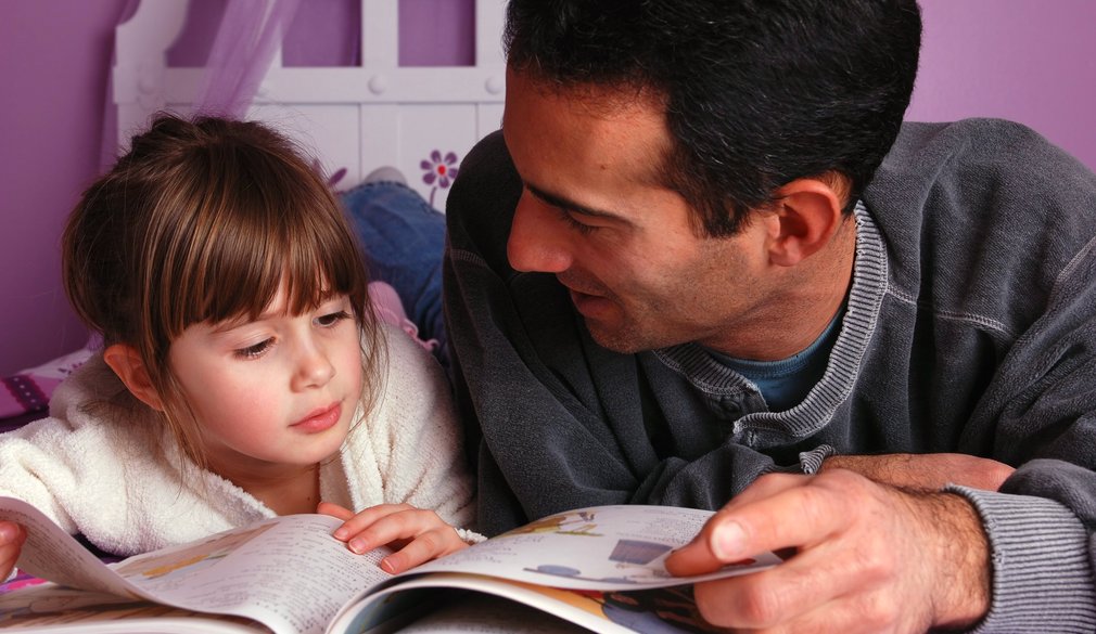 Vater und Tochter liegen auf dem Bett und schauen ein Buch an.