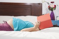 Schwangere liegt auf dem Bett und liest ein Buch