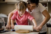 Mutter hilft kleinkind Mädchen in der Küche einen Kuchenteig auszurollen