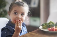Kleines Mädchen isst Gemüse mit der Hand
