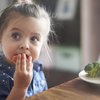 Kleines Mädchen isst Gemüse mit der Hand