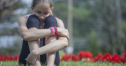 Tennager Mädchen umfasst ihre Knie: mit Liebeskummer auf Wiese