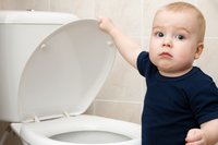 Kleiner Junge hebt Toilettendeckel hoch und guckt irritiert.