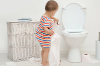 Kleinkind steht an der Toilette und übt mit Klopapier.