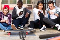 Vier Jugendliche auf dem Bürgersteig an ihren Smartphones