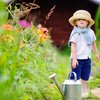 Kleinkind steht im Garten hat großen Hut auf mit Gießkanne