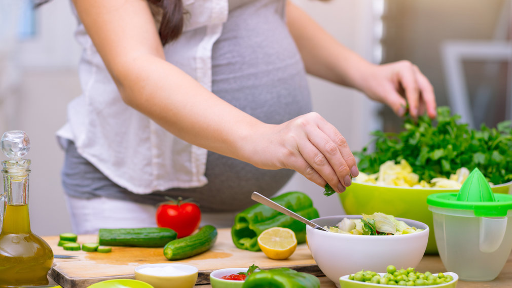 Schwangere Frau bereitet gesundes Essen vor.