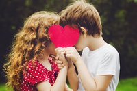 Verliebte Kinder halten Herz vor ihre Gesichter