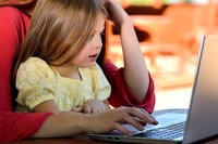 Kleines Mädchen sitzt mit ihrer Mutter vorm Laptop.