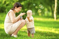 Mutter und Baby spielen im Freien mit Seifenblasen
