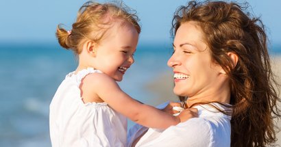 Mutter mit Tochter auf Arm am Strand 