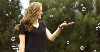 Lächelnde Frau draußen umgeben un Seifenblasen und hält eine auf der Hand