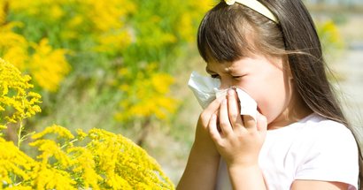 Schulkind mit Allergie putzt sich die Nase vor gelben Blumen