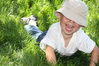 Junge liegt im Gras. Hut verdeckt seine Augen. Lustig
