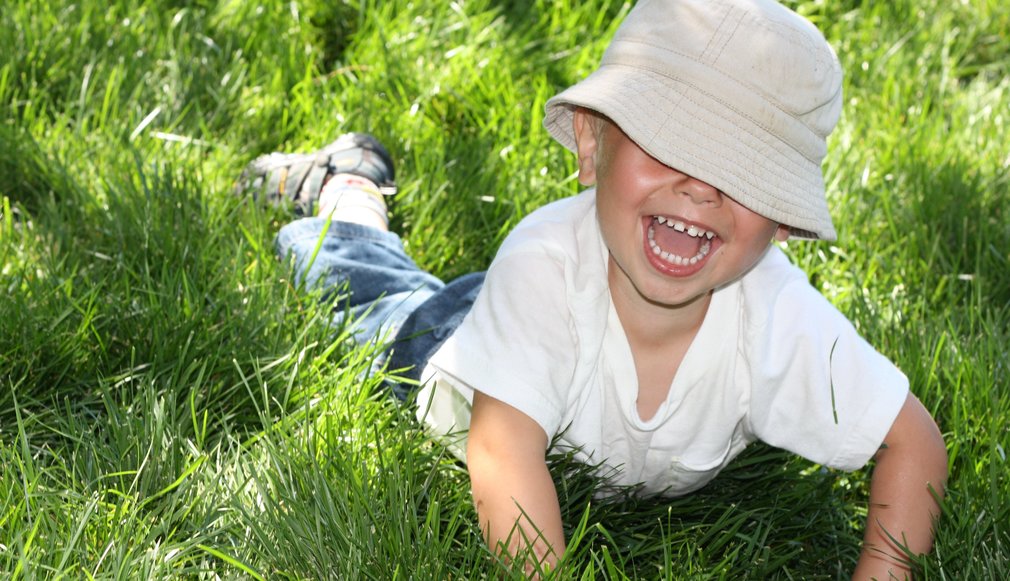 Junge liegt im Gras. Hut verdeckt seine Augen. Lustig