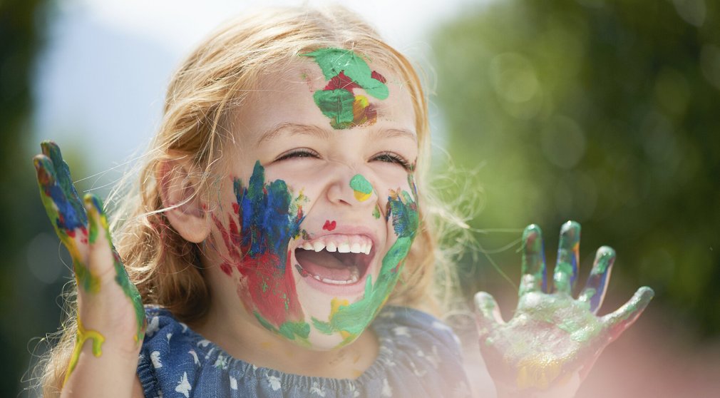 Kreativität: Kind beim Malen mit Farbe im Gesicht