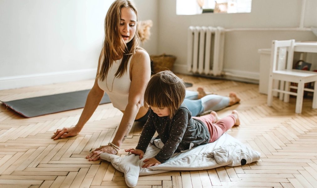 Mutter und kleine Tochter machen gemeinsam Gymnastik im Wohnzimmer.