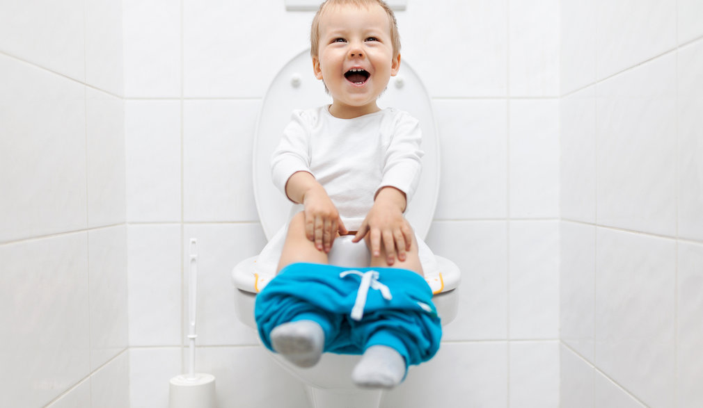 Kleinkind sitzt auf der Toilette und freut sich.