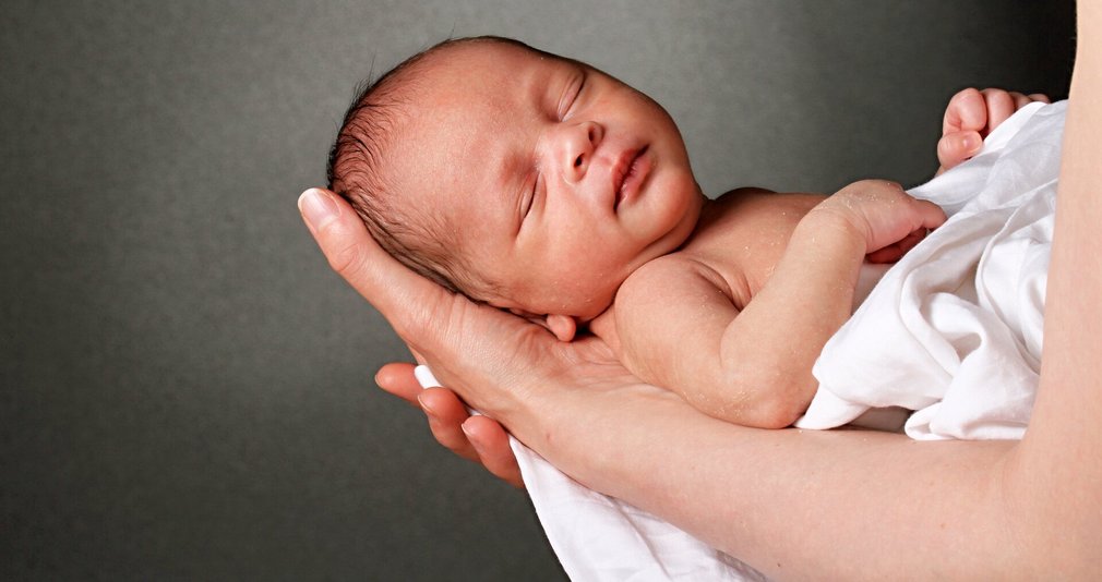 Neugeborenes schläft auf Händen der Mutter.