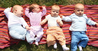 4 Babys liegen auf einer Decke auf einer Wiese