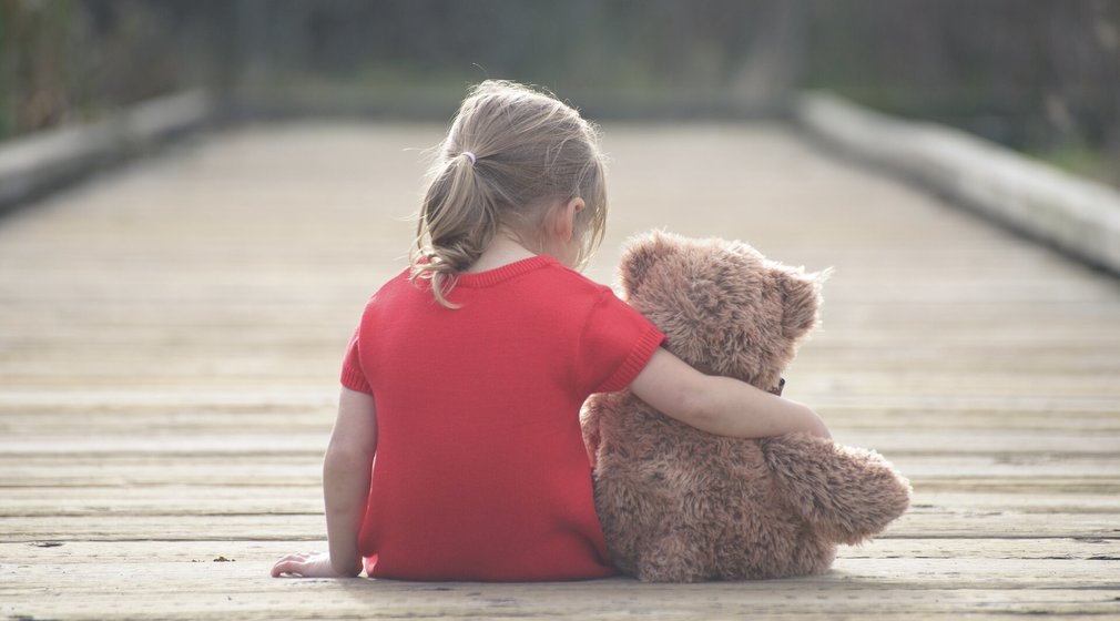 Kleines Mädchen sitzt mit Teddy-Bären auf einem Steg