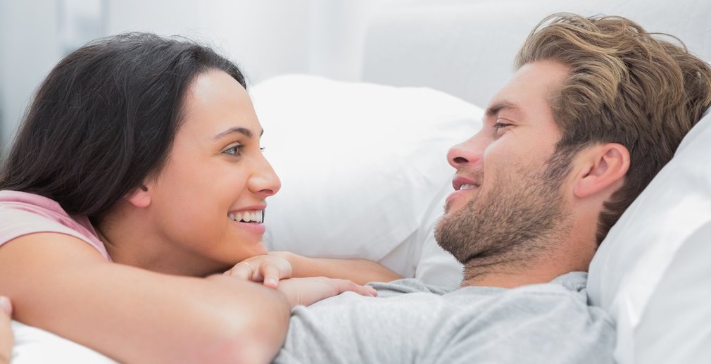 Mann und Frau lachen einander an im Bett 